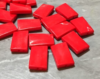 Puede incluir: Un grupo de cuentas rectangulares de color rojo brillante, probablemente hechas de plástico o vidrio, con un agujero en el centro de cada cuenta. Estas cuentas son perfectas para la elaboración de joyas o proyectos de manualidades.