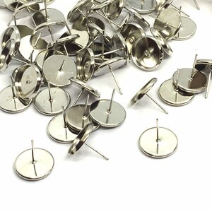 May include: A pile of silver-toned earring settings with round bezels. The settings are designed to hold a cabochon or other flat-backed embellishment.