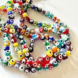 May include: Strands of colorful glass beads with an eye-like design. The beads are in various colors, including red, yellow, blue, green, and white. The beads are strung together, creating a decorative accessory.