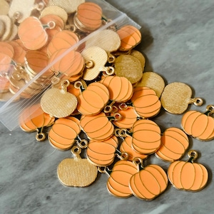 Könnte beinhalten: Eine Tüte mit goldfarbenen Metall-Kürbis-Anhängern. Die Anhänger sind etwa 2,5 cm im Durchmesser und haben eine Öse zum Aufhängen. Die Anhänger sind perfekt, um Ihren Bastelarbeiten einen Hauch von Herbst zu verleihen.