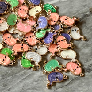 Könnte beinhalten: Eine Sammlung farbenfroher, geisterförmiger Anhänger mit goldfarbenen Metallkanten. Die Anhänger sind in verschiedenen Farben erhältlich, darunter Rosa, Grün, Lila und Weiß, mit schwarzen Punktaugen. Ideal für Schmuckherstellung oder andere Bastelprojekte.