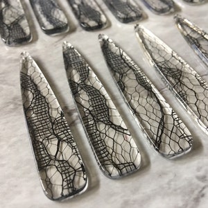 May include: A set of clear, long, narrow, decorative pieces with a black lace pattern inside. The pieces are arranged in a row on a white surface.