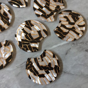 May include: A set of eight white, black, and gold half-circle shaped resin embellishments with a geometric pattern.