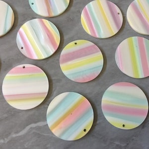 May include: A collection of 10 round, iridescent, pastel-colored, striped, decorative ornaments with a hole in the center.