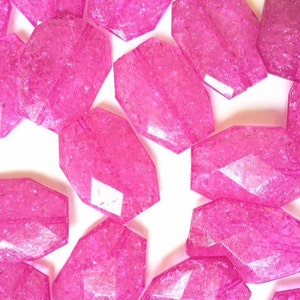 May include: A group of pink faceted glass beads with a sparkly finish. The beads are oval shaped and have a slightly irregular surface.