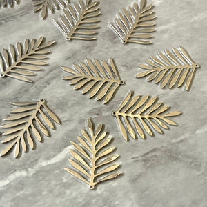 May include: A collection of silver-colored metal palm leaf charms. The leaves are detailed and have a shiny finish.