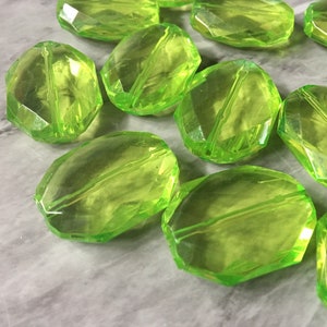 May include: A group of lime green faceted glass beads. The beads are oval shaped and have a hole in the center for stringing.