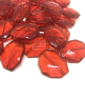 May include: A collection of faceted, reddish-orange acrylic beads. The beads are irregularly shaped with multiple flat surfaces, creating a sparkling effect. Ideal for jewelry making or craft projects.