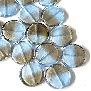 May include: A collection of round, glass beads with a split color design. Each bead is divided into two halves, one half is a light blue color and the other half is a metallic silver color. The beads are scattered on a white surface.