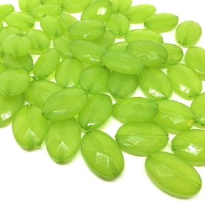 May include: A collection of translucent, lime green oval beads with faceted surfaces. These beads are scattered against a white background, showcasing their shape and color. Ideal for jewelry making and crafting.