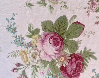 May include: A pink fabric with a floral pattern featuring pink, red, and green roses, and blue and yellow flowers.