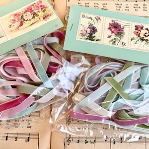 May include: An assortment of pastel-colored velvet ribbons in shades of pink, green, and lavender, alongside vintage floral-themed ephemera. The ribbons are packaged in clear plastic, and the background features sheet music and vintage postage stamp images.
