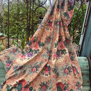 Puede incluir: Una pieza de tela con fondo crema y un patr&oacute;n repetitivo de flores rosas, rojas y moradas, hojas verdes y detalles de volutas en color canela. El tejido tambi&eacute;n muestra finas rayas diagonales oscuras en todo el dise&ntilde;o.