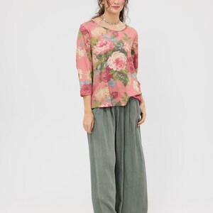 Puede incluir: Una blusa rosa con estampado floral, mangas tres cuartos y cuello redondo. Combinada con pantalones de pierna ancha verde oliva y bailarinas negras. La blusa presenta un gran estampado de rosas en tonos rosa, rojo y crema.