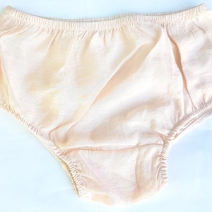 May include: A pair of pale peach-colored baby bloomers with a gathered elastic waistband.