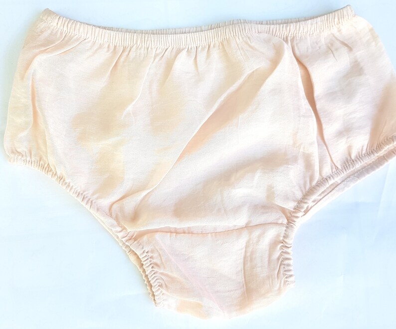 May include: A pair of pale peach-colored baby bloomers with a gathered elastic waistband.