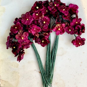 May include: A bunch of burgundy velvet flowers with yellow centers, attached to green stems. The flowers are arranged in a bouquet shape.