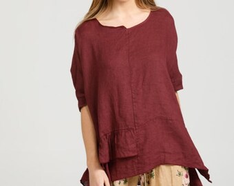 Puede incluir: Una blusa de lino color burdeos con un dobladillo con volantes y un diseño ligeramente asimétrico. La blusa se combina con pantalones beige con estampado floral.