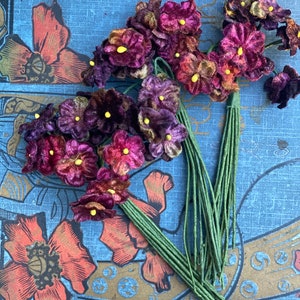 Puede incluir: Un ramo de flores de terciopelo morado con centros amarillos. Las flores est&aacute;n unidas a tallos verdes.