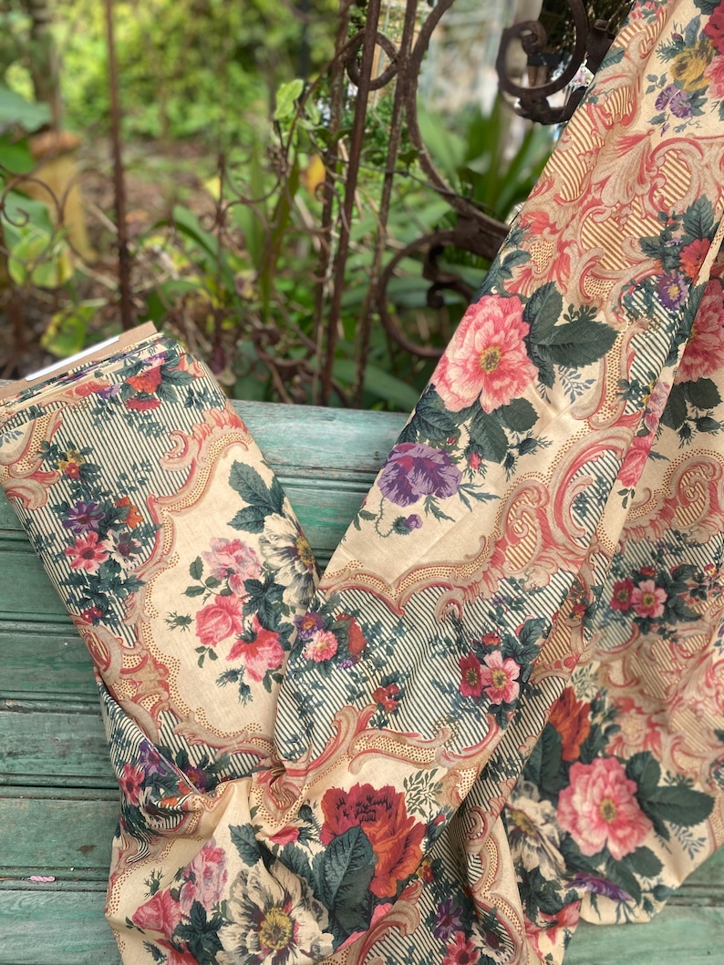 Puede incluir: Una pieza de tela con fondo color crema y un patr&oacute;n repetitivo de ramos de flores rosas, rojas y moradas. El dise&ntilde;o incluye bordes ornamentados de color beige y finas rayas verticales de color verde oscuro entre los motivos.