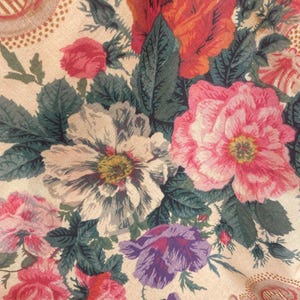 Puede incluir: Una tela con un denso estampado floral sobre un fondo beige claro. El dise&ntilde;o incluye grandes flores detalladas en tonos rojo vibrante, rosa suave, blanco y morado, acentuadas por hojas y tallos de color verde oscuro con texturas complejas.