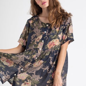 Puede incluir: Un vestido corto de manga corta, de color azul marino con estampado floral, con cierre de botones en la parte delantera. El vestido tiene un corte holgado y una falda fruncida.