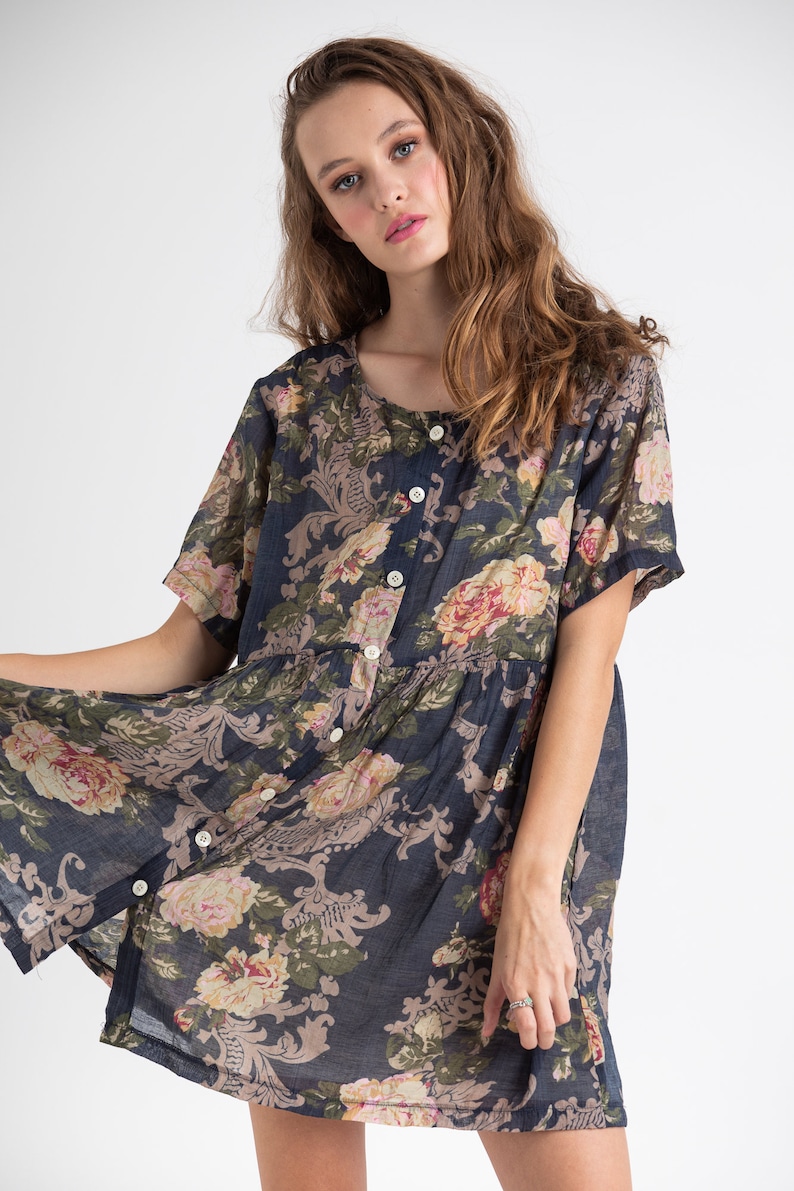 Puede incluir: Un vestido corto de manga corta, de color azul marino con estampado floral, con cierre de botones en la parte delantera. El vestido tiene un corte holgado y una falda fruncida.