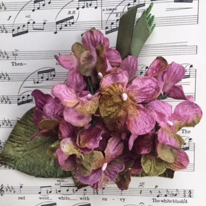May include: A cluster of pink and green velvet flowers with a green leaf stem. The flowers are arranged in a bouquet and have a soft, velvety texture.