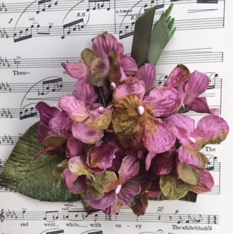 May include: A cluster of pink and green velvet flowers with a green leaf stem. The flowers are arranged in a bouquet and have a soft, velvety texture.