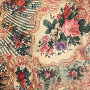 Puede incluir: Una tela con un patr&oacute;n repetitivo de ramos de flores en tonos rosa, rojo y morado, sobre un fondo crema. El dise&ntilde;o incluye bordes con volutas intrincadas y secciones de finas rayas verticales de color verde oscuro y crema.