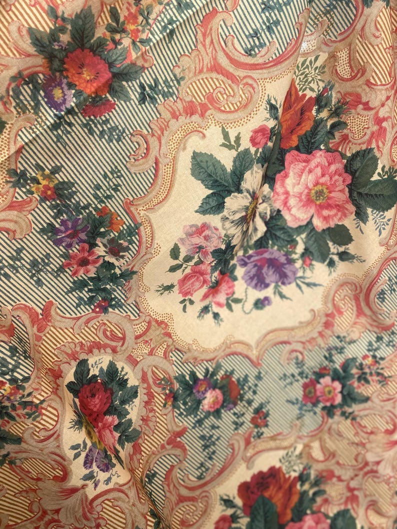 Puede incluir: Una tela con un patr&oacute;n repetitivo de ramos de flores en tonos rosa, rojo y morado, sobre un fondo crema. El dise&ntilde;o incluye bordes con volutas intrincadas y secciones de finas rayas verticales de color verde oscuro y crema.