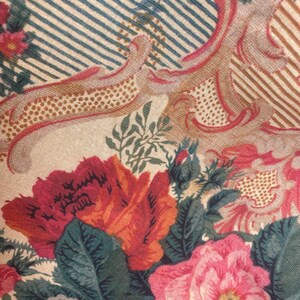 Puede incluir: Una tela con un estampado floral de grandes flores rojas, rosas y blancas, hojas verdes y elementos decorativos en color tostado. El fondo consiste en finas rayas diagonales alternas en azul y blanco, creando un efecto visual.