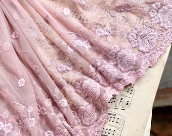 Op de afbeelding: Roze bloemenkant met een delicaat geborduurd ontwerp. De kant is gedrapeerd over een blad muziek.