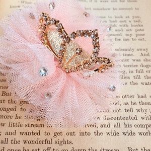 Pode incluir: Uma delicada flor de tule rosa com um prendedor de cabelo de borboleta dourado adornado com strass brilhantes. A borboleta tem um acabamento brilhante e &eacute; um belo acento para qualquer penteado.
