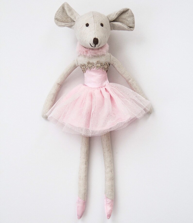 May include: A gray and white fabric mouse doll wearing a pink tulle tutu with a gold trim. The doll has long legs and is standing on a white background.