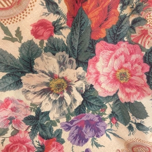 Puede incluir: Una tela con un denso estampado floral sobre un fondo beige claro. El dise&ntilde;o incluye grandes flores detalladas en tonos rojo vibrante, rosa suave, blanco y morado, acentuadas por hojas y tallos de color verde oscuro con texturas complejas.