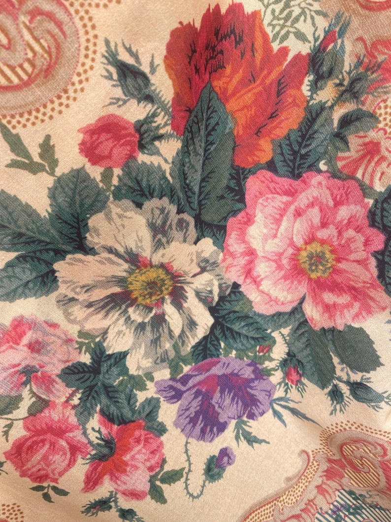 Puede incluir: Una tela con un denso estampado floral sobre un fondo beige claro. El dise&ntilde;o incluye grandes flores detalladas en tonos rojo vibrante, rosa suave, blanco y morado, acentuadas por hojas y tallos de color verde oscuro con texturas complejas.