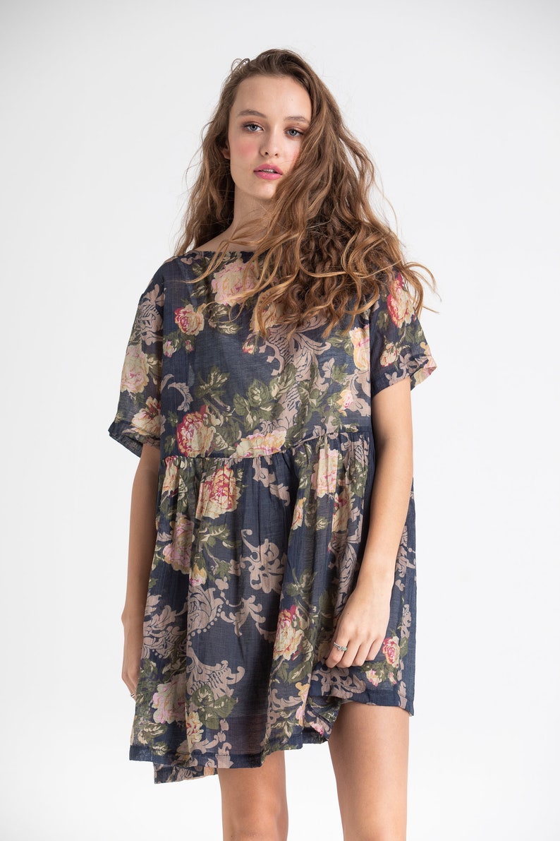 Puede incluir: Un vestido azul marino de manga corta con estampado floral. El vestido tiene un corte holgado y una cintura fruncida.