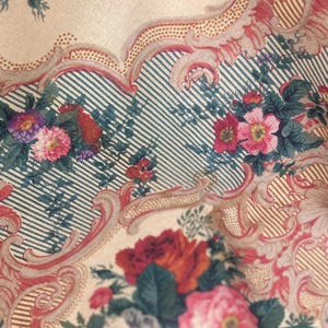 Puede incluir: Una tela con un patr&oacute;n floral de flores rosas, rojas y moradas sobre un fondo crema. El dise&ntilde;o incluye bordes intrincados de volutas en un tono rojo apagado y secciones de finas rayas verticales de color azul oscuro sobre fondo crema.