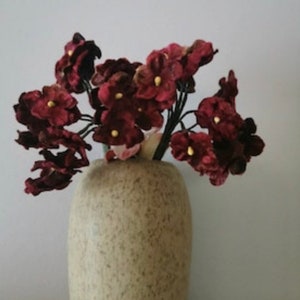 May include: A bouquet of burgundy velvet flowers in a speckled beige vase. The flowers have a delicate, almost delicate, appearance.