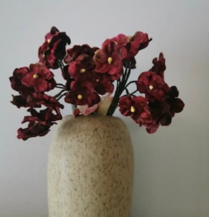 May include: A bouquet of burgundy velvet flowers in a speckled beige vase. The flowers have a delicate, almost delicate, appearance.