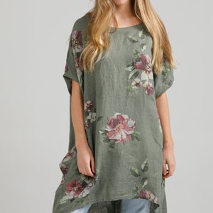 May include: A green linen tunic with a floral print featuring pink, white, and purple flowers. The tunic has a relaxed fit and a high-low hemline.