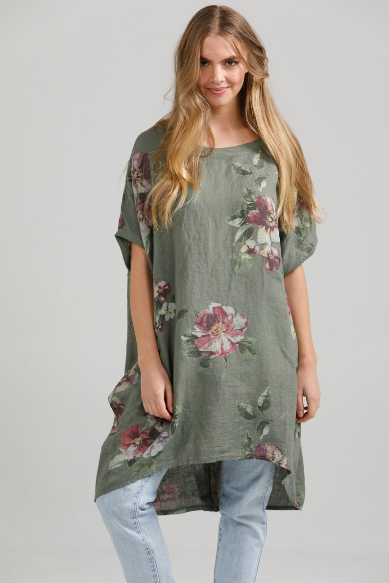 May include: A green linen tunic with a floral print featuring pink, white, and purple flowers. The tunic has a relaxed fit and a high-low hemline.