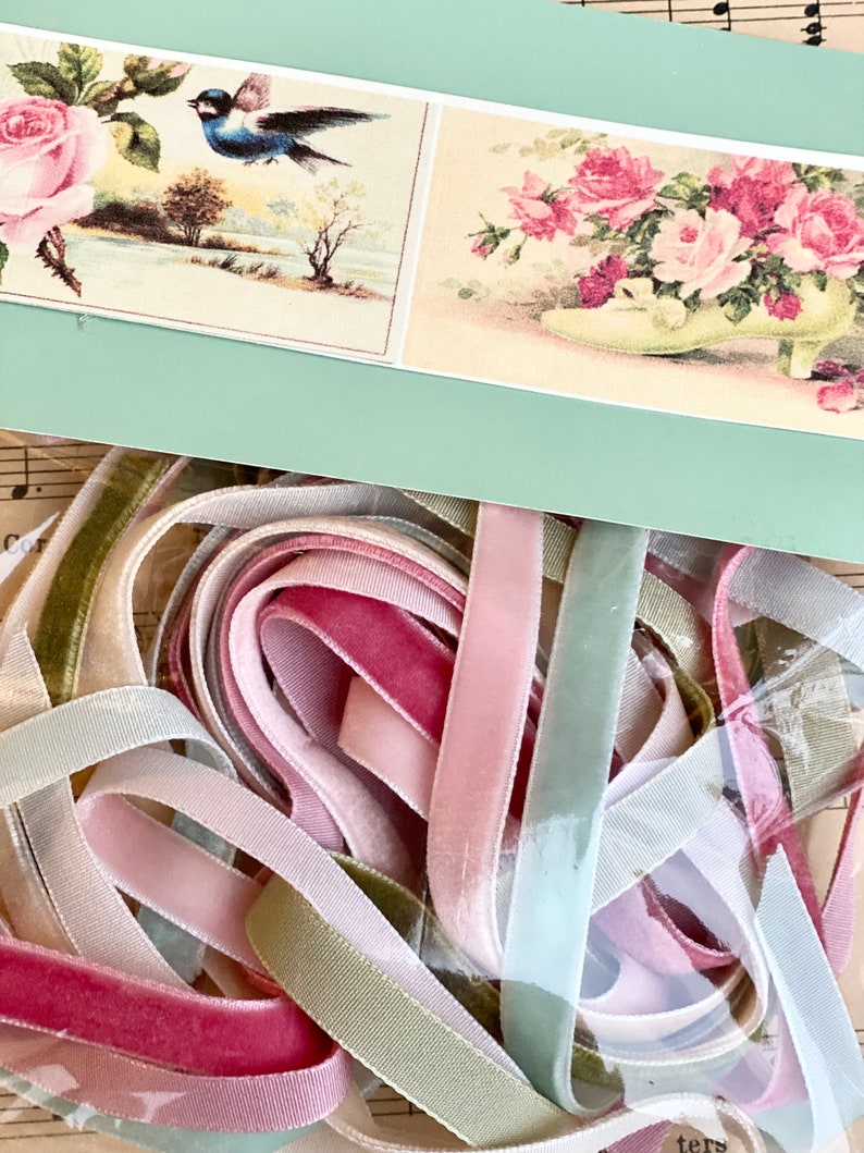 May include: A collection of pastel-colored velvet ribbons in shades of pink, green, and cream. Above, a light green card displays vintage floral illustrations, including roses and a bird. The ribbons are bundled together.