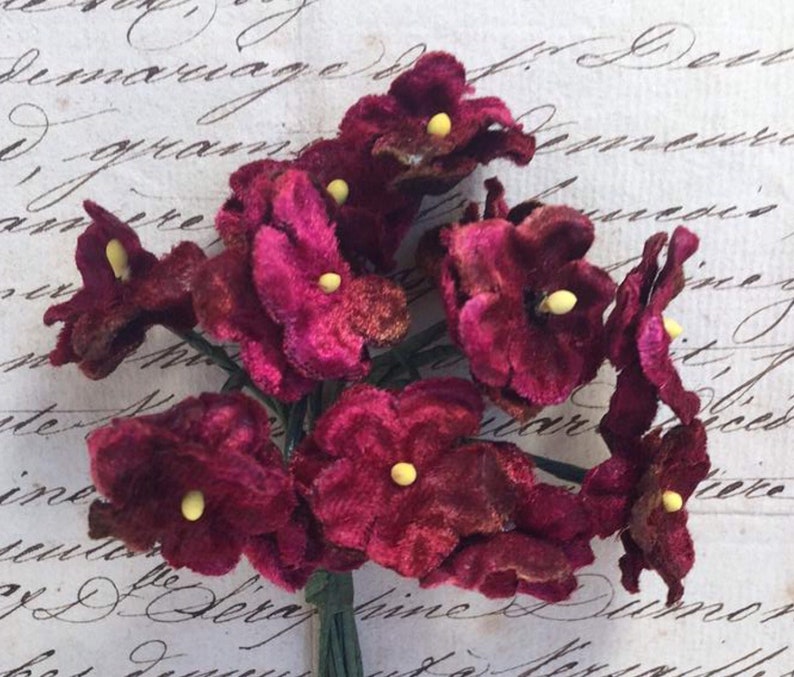 May include: A bunch of burgundy velvet flowers with yellow centers. The flowers are arranged in a bouquet and are ready to be used for crafting or decorating.