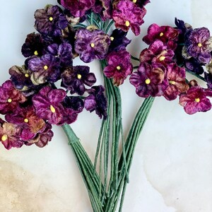 Puede incluir: Un ramo de flores de terciopelo morado con centros amarillos. Las flores est&aacute;n unidas a tallos verdes.