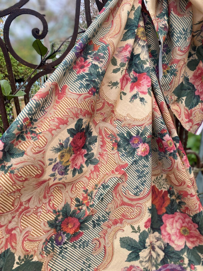 Puede incluir: Una tela textil con fondo beige y un patr&oacute;n repetitivo de ramos de flores en tonos rojo, rosa y morado vibrantes. El dise&ntilde;o incluye bordes con volutas intrincadas y finas rayas de color verde oscuro, creando un efecto visual superpuesto.