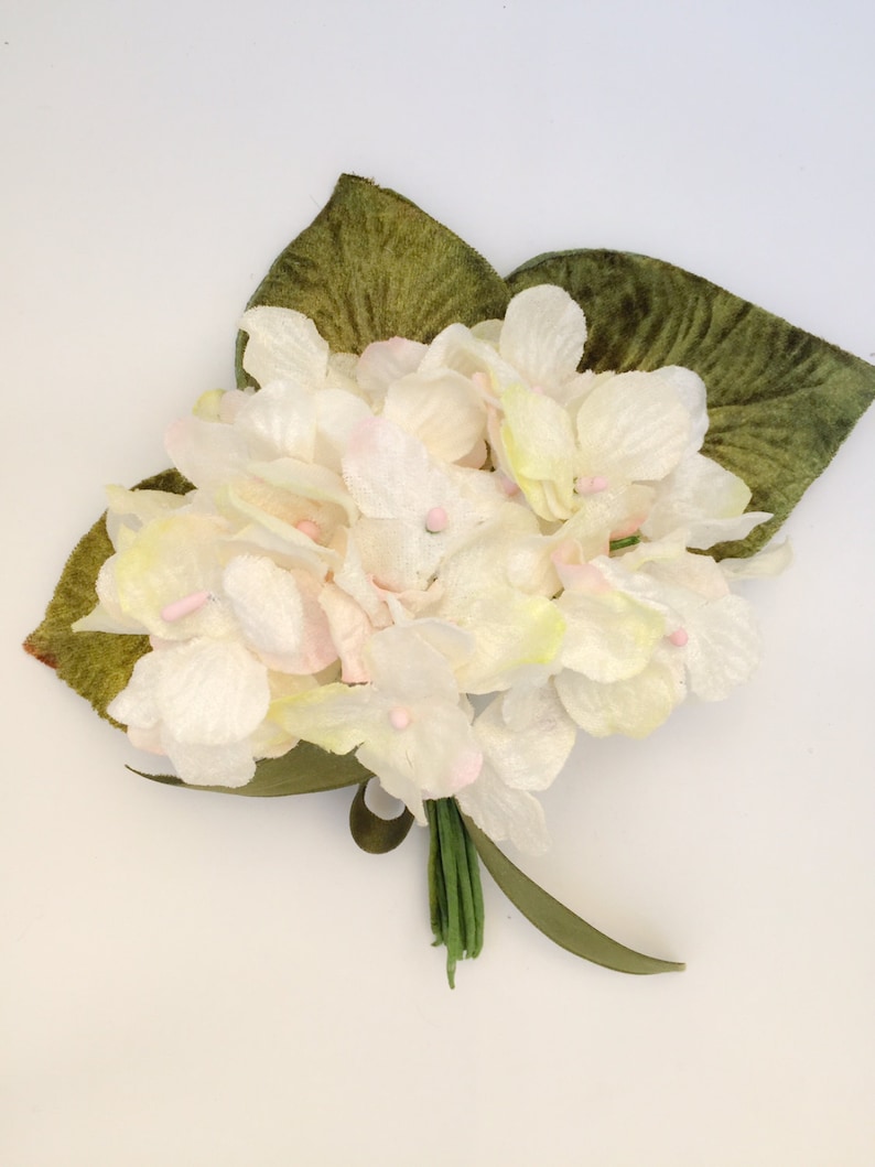May include: A bouquet of white and light pink felt flowers with green felt leaves. The flowers have a delicate, vintage look.
