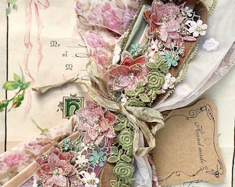 May include: A collection of vintage fabric scraps, lace, and ribbon in shades of pink, green, and white. The fabric scraps are arranged in a bouquet-like shape and tied with a brown ribbon. A small tag reads "Hand made" and "Miniature".
