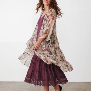 May include: A dark plum midi dress with a tiered skirt and lace trim, paired with a sheer, open-front duster cardigan featuring a vintage-inspired rose floral print and script text. Dark velvet Mary Jane flats with bows complete the ensemble.
